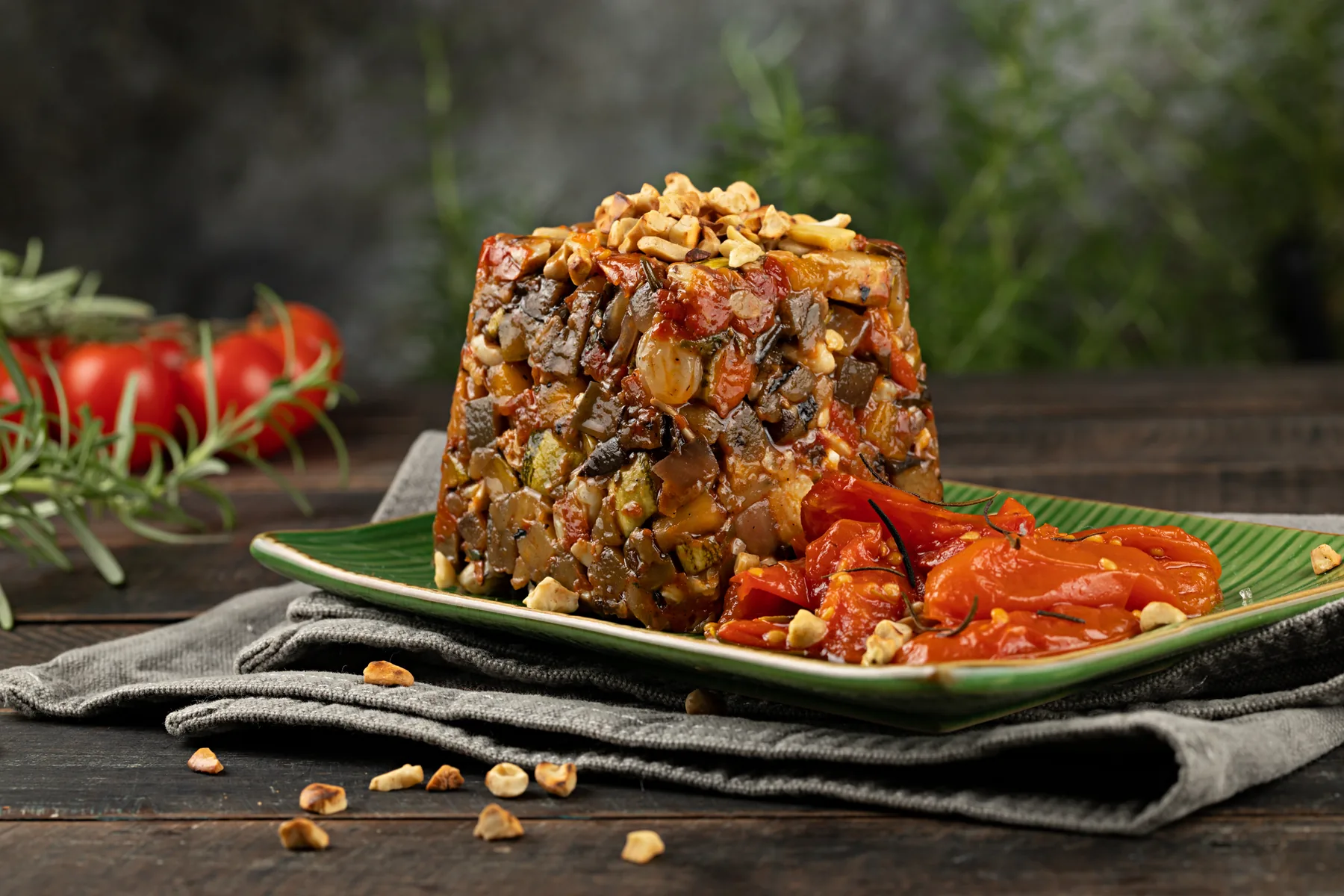 Caponata mediterrânea desenformada sobre folha verde, com castanhas por cima e tomates ao lado