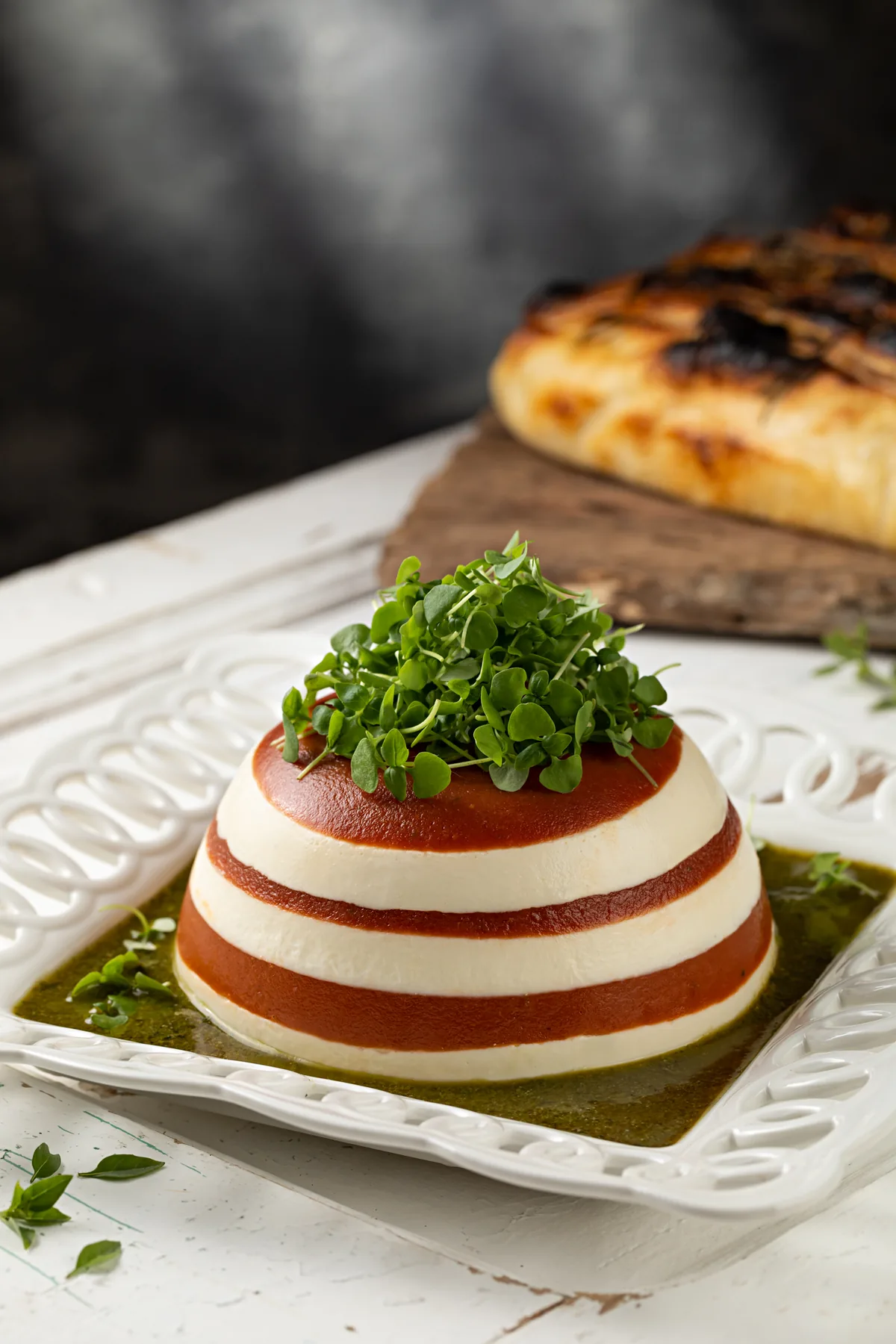 Esfera caprese em camadas brancas e vermelhas, com brotos verdes no topo, sobre pesto