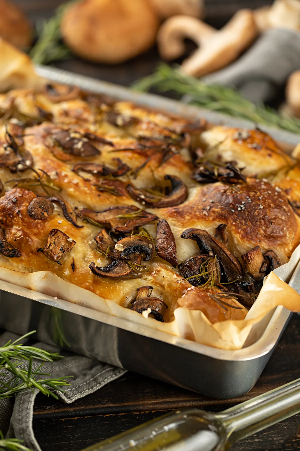 Focaccia na forma coberta de cogumelos fatiados e ramos de alecrim